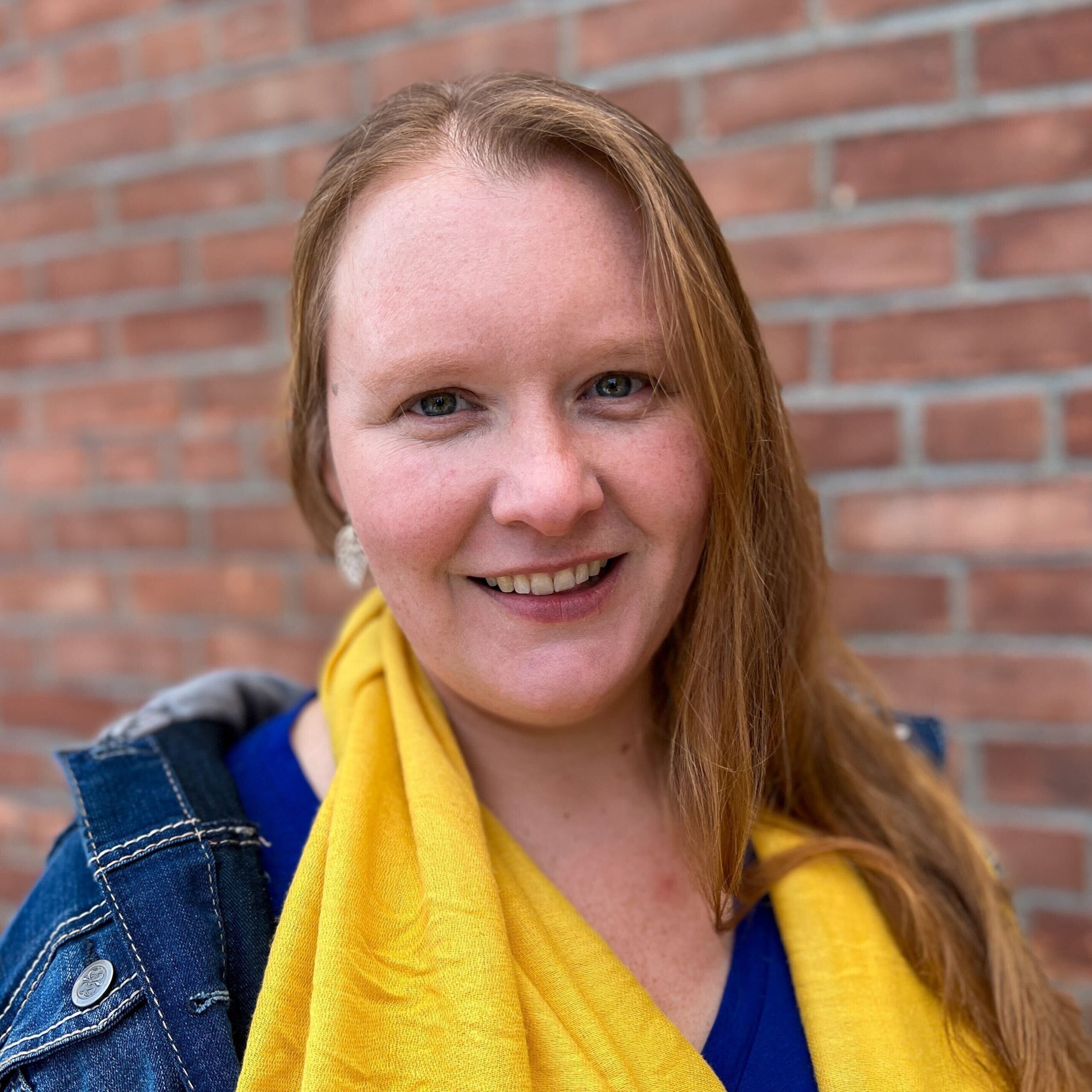 Woman with red hair, a yellow scarf, and blue shirt smiling